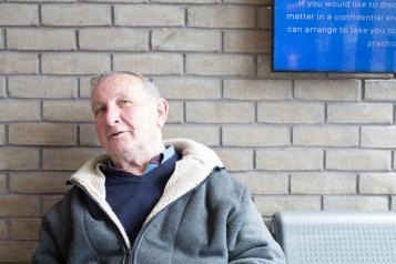 Man sat next to a wall on a bench