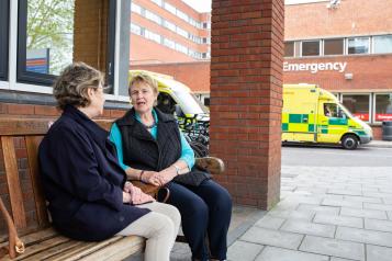 Two ladies talking outside a hospital with an ambulance behind them 