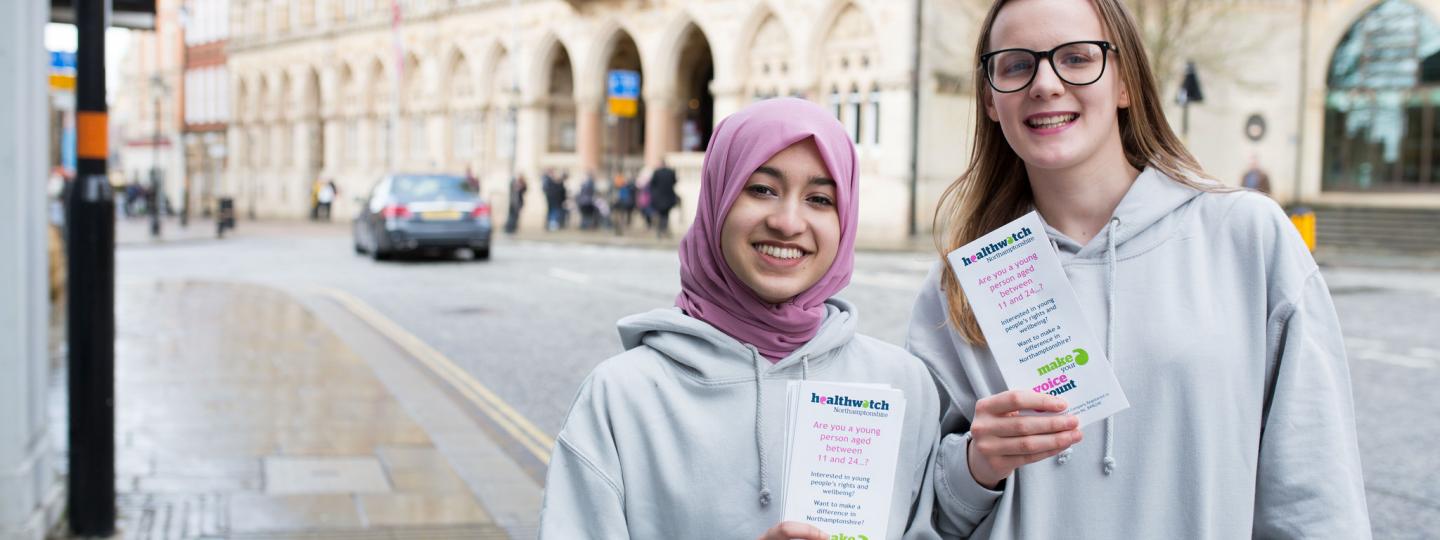Two young female volunteers holding Healthwatch leaflets